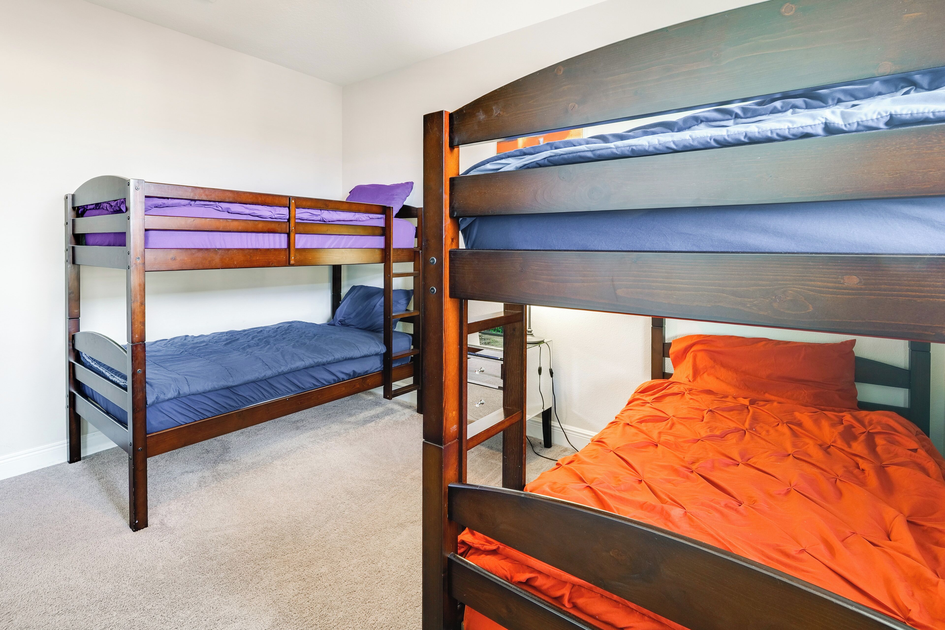 Una camera con letto a castello in legno, pavimento rivestito di moquette e una scrivania con lampada.