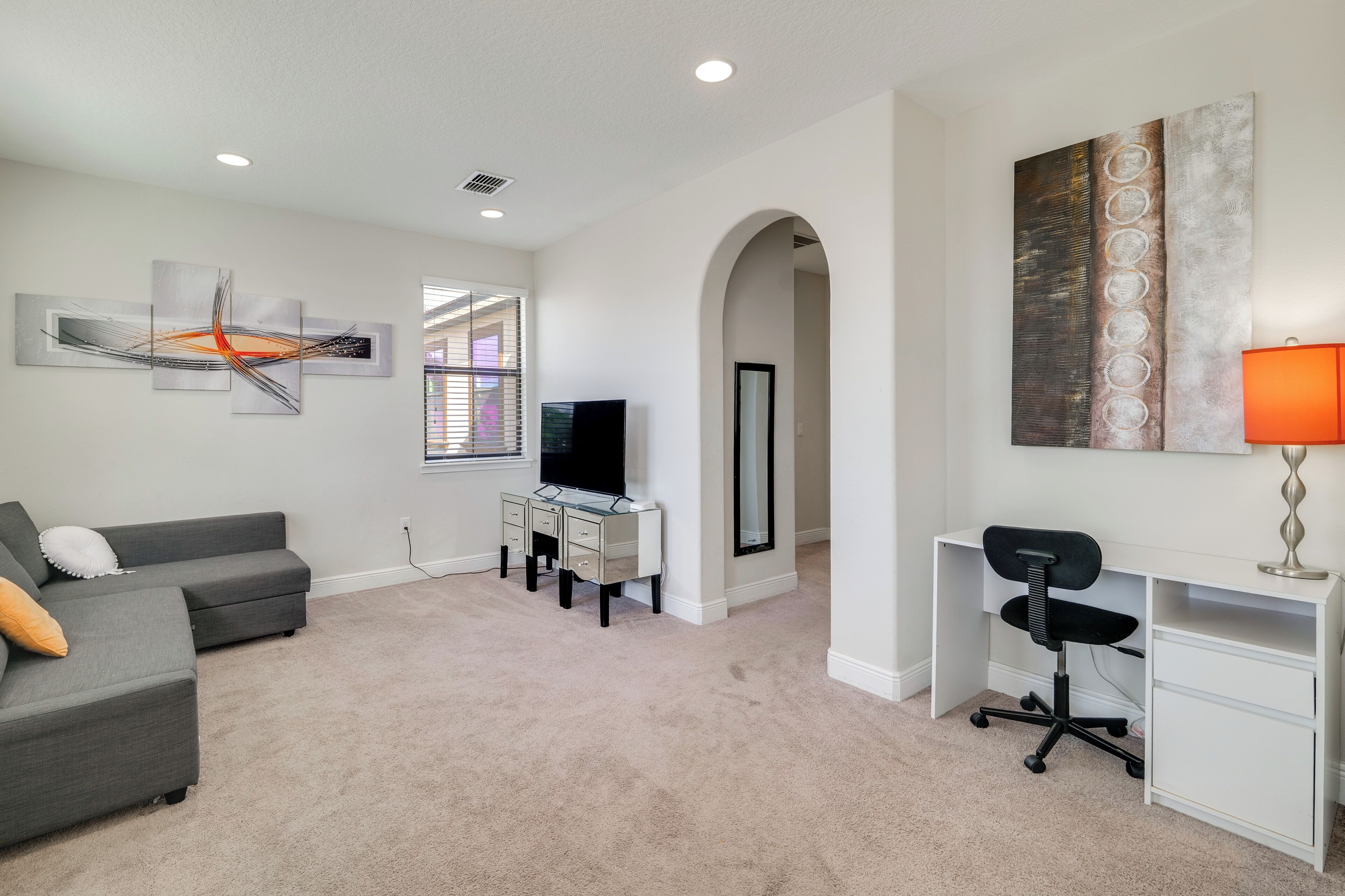 A modern living room with a grey sectional sofa, a glass desk, a black office chair, and a TV.