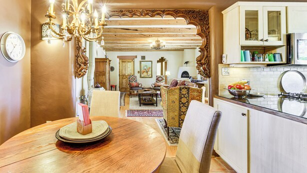 Un comedor con una mesa de madera, sillas y una araña. Cuenta con una zona de cocina con armarios y un microondas.
