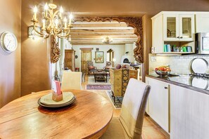 A dining area with a wooden table, chairs, and a chandelier. There is a kitchen area with cabinets and a microwave. - 14 Mi to Taos Ski Valley: Mtn-view Gem w/ Patio! (El Prado)