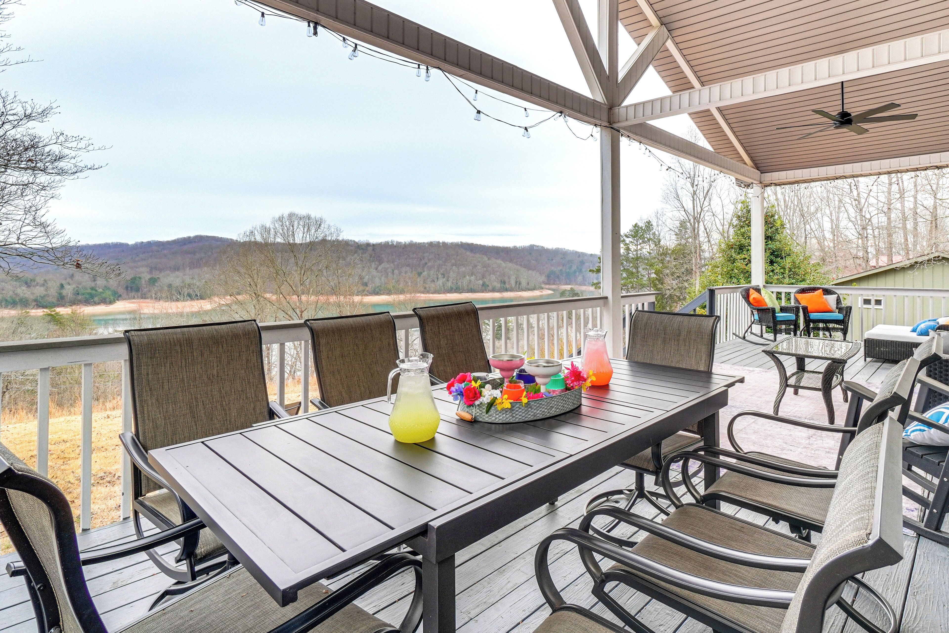 A covered outdoor dining area with a table and chairs, a pitcher of lemonade, and a basket of colorful flowers.