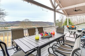 Un espace extérieur abrité, aménagé pour prendre les repas, avec une table et des chaises, une carafe de limonade et un panier rempli de fleurs aux couleurs vives.