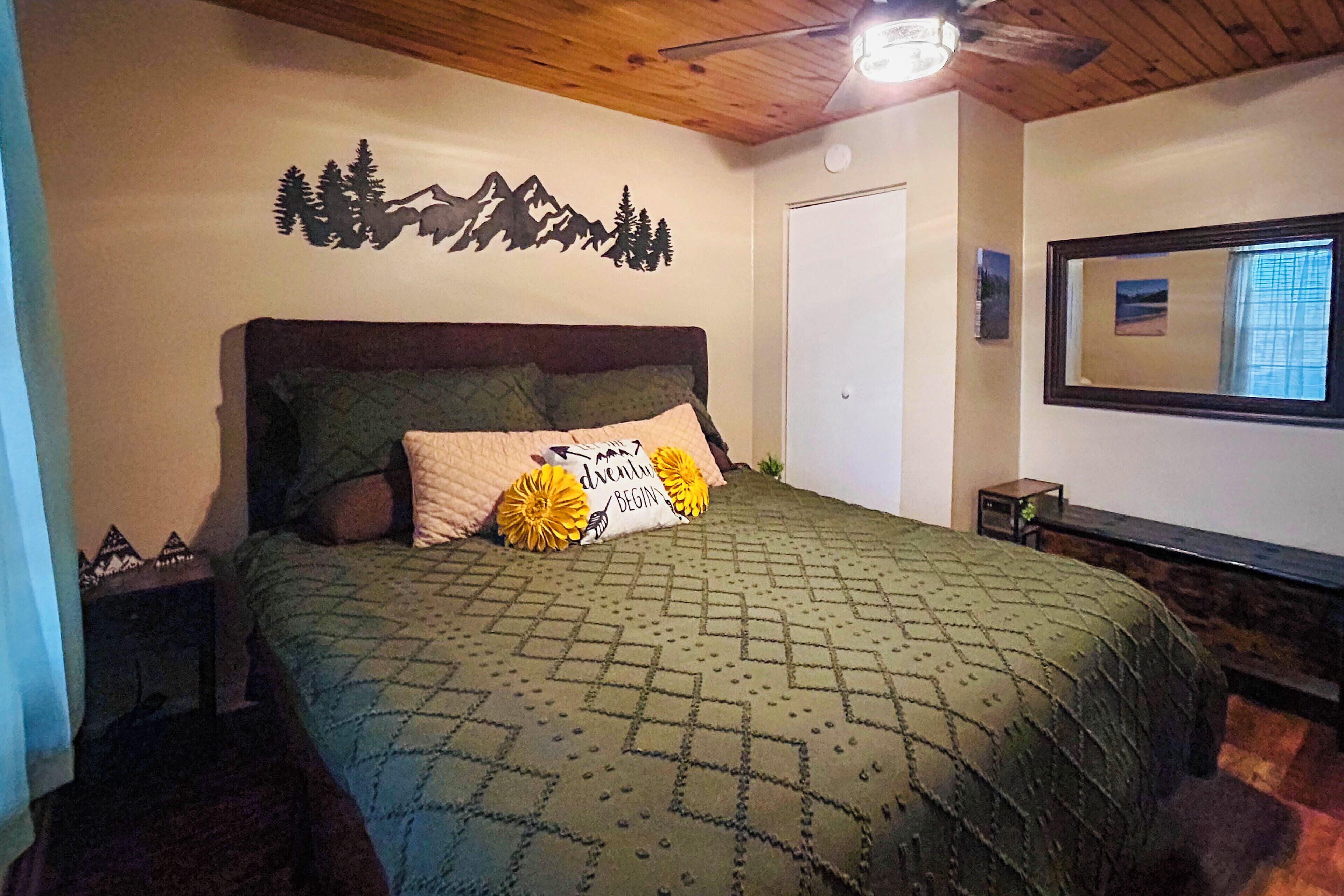 A bedroom with a bed, a headboard, a wall-mounted mirror, a door, and a small bedside table.