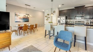 Una cucina moderna con mobili scuri, un'isola centrale e una zona pranzo con sedie in legno e una televisione.