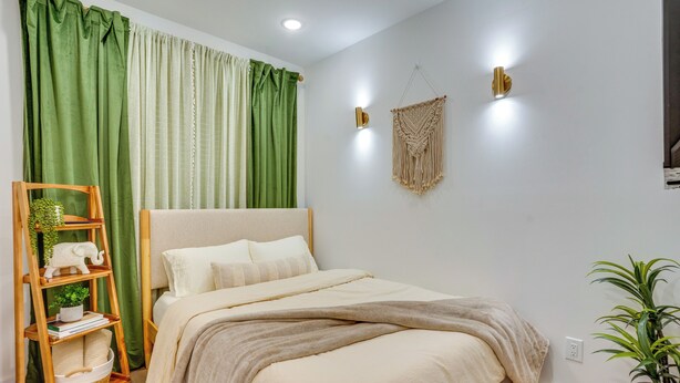 A bedroom with a bed, a wooden ladder shelf, a macrame wall hanging, and a potted plant. - Spacious & Upscale Family Retreat: 5 Mi to NYC (Jersey City)