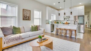 A modern living room with a sofa, coffee table, and a kitchen area with a dining bar. - Spacious & Upscale Family Retreat: 5 Mi to NYC (Jersey City)