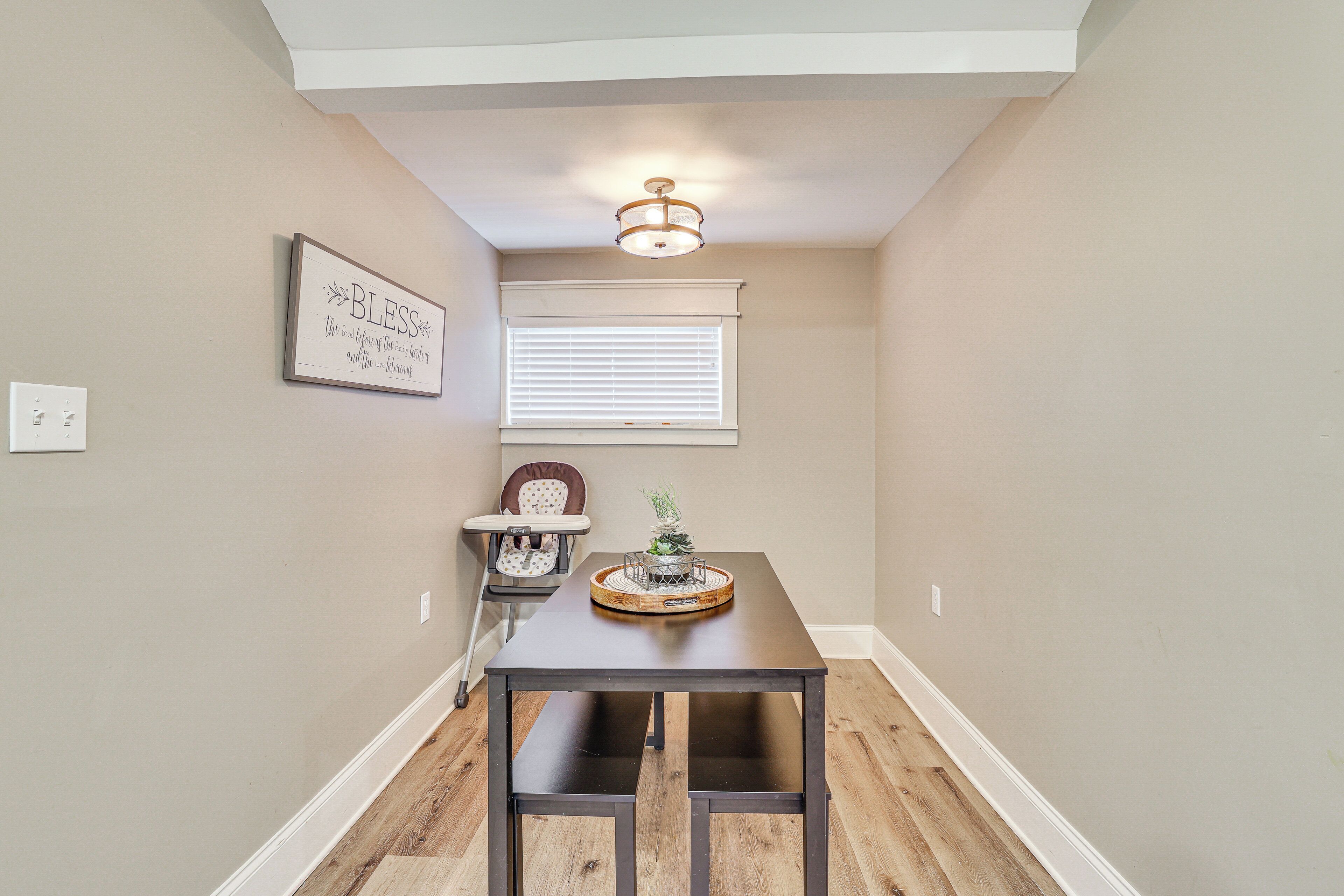 A dining area with a table, chairs, a ceiling light, a window with blinds, and a wall-mounted sign.