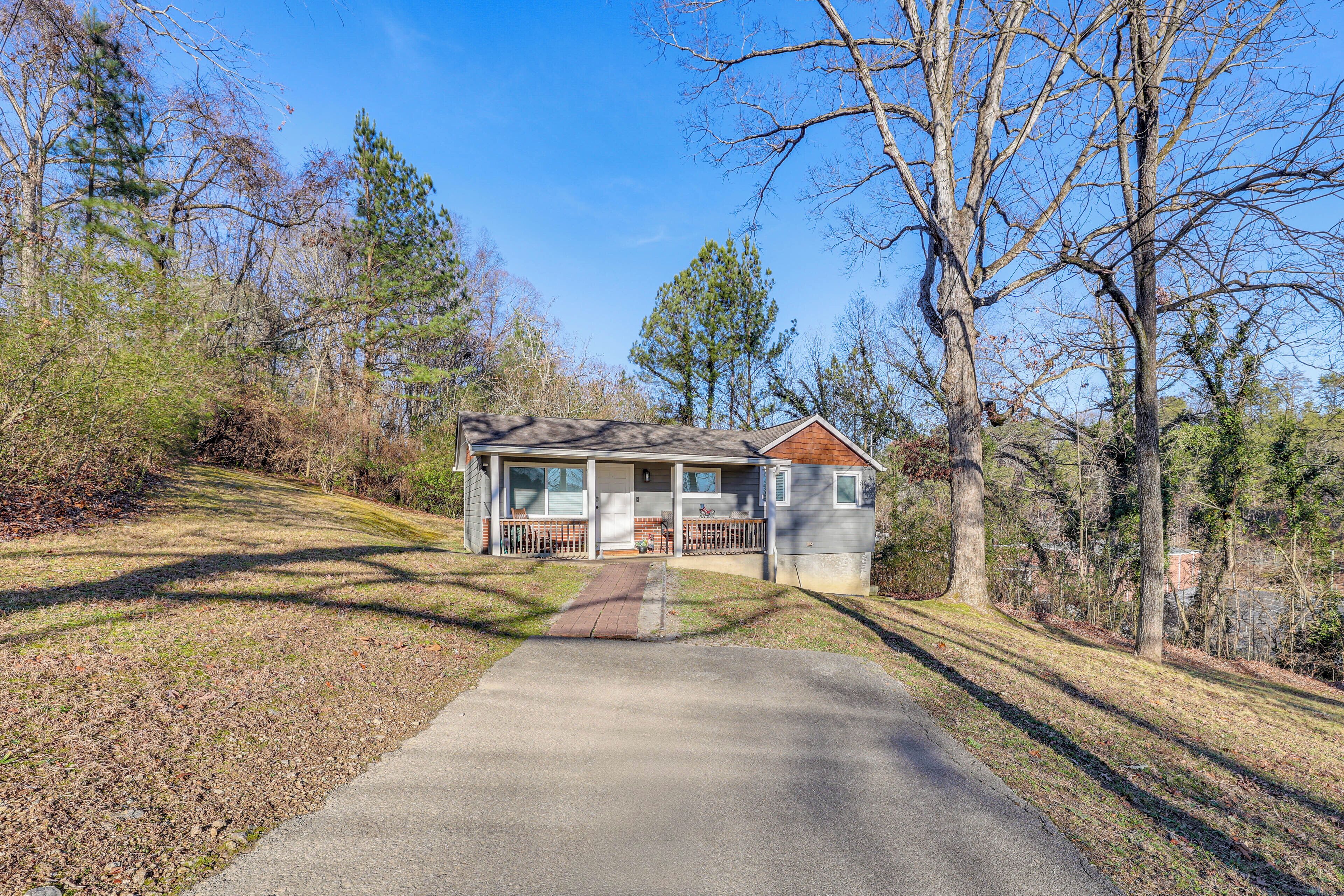 A small, single-story house with a front porch, surrounded by trees and a clear sky.