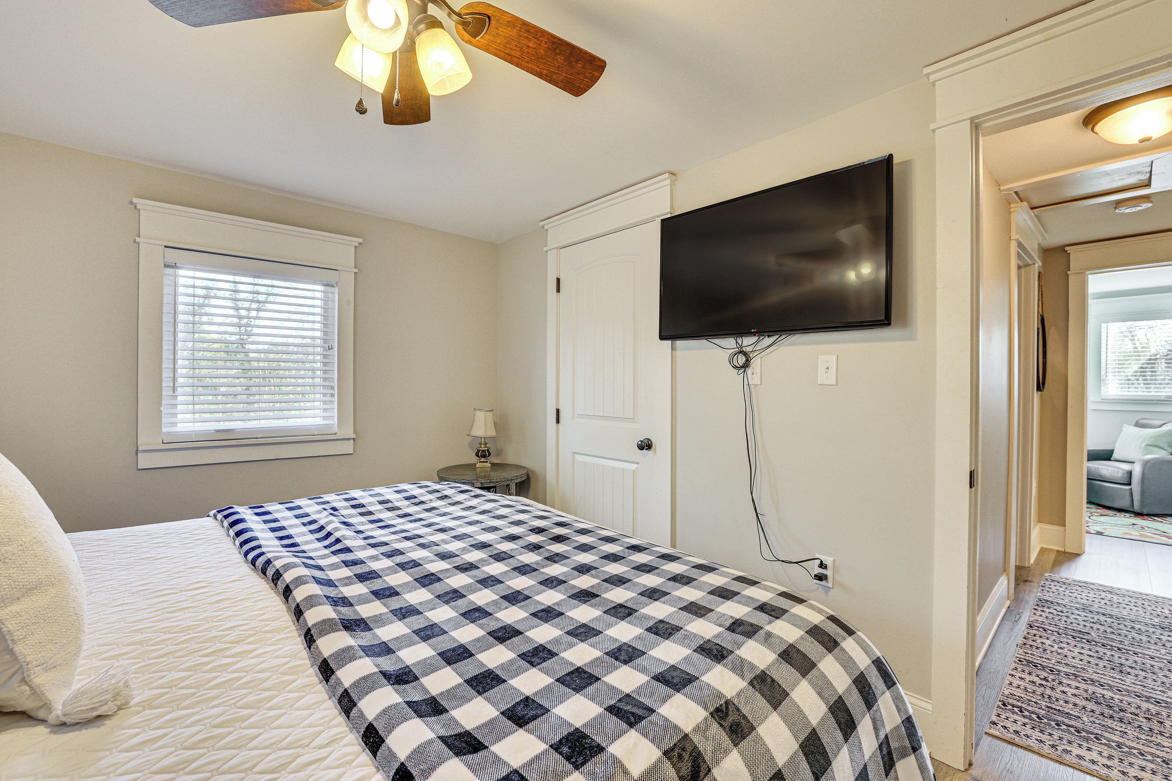 Une chambre à coucher comprenant un lit, un ventilateur de plafond, un téléviseur fixé au mur et une porte donnant sur une autre pièce.