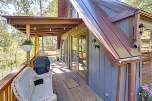 A wooden deck with a covered seating area, a grill, and a potted plant. - Serene Black Hills Forest Cabin w/ Wraparound Deck (Rapid City)