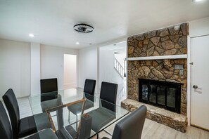 A modern living room with a glass-top dining table, black chairs, a stone fireplace, and a staircase leading to another level. - Family + Pet Friendly! Garland Home w/ Fenced Yard (Garland)