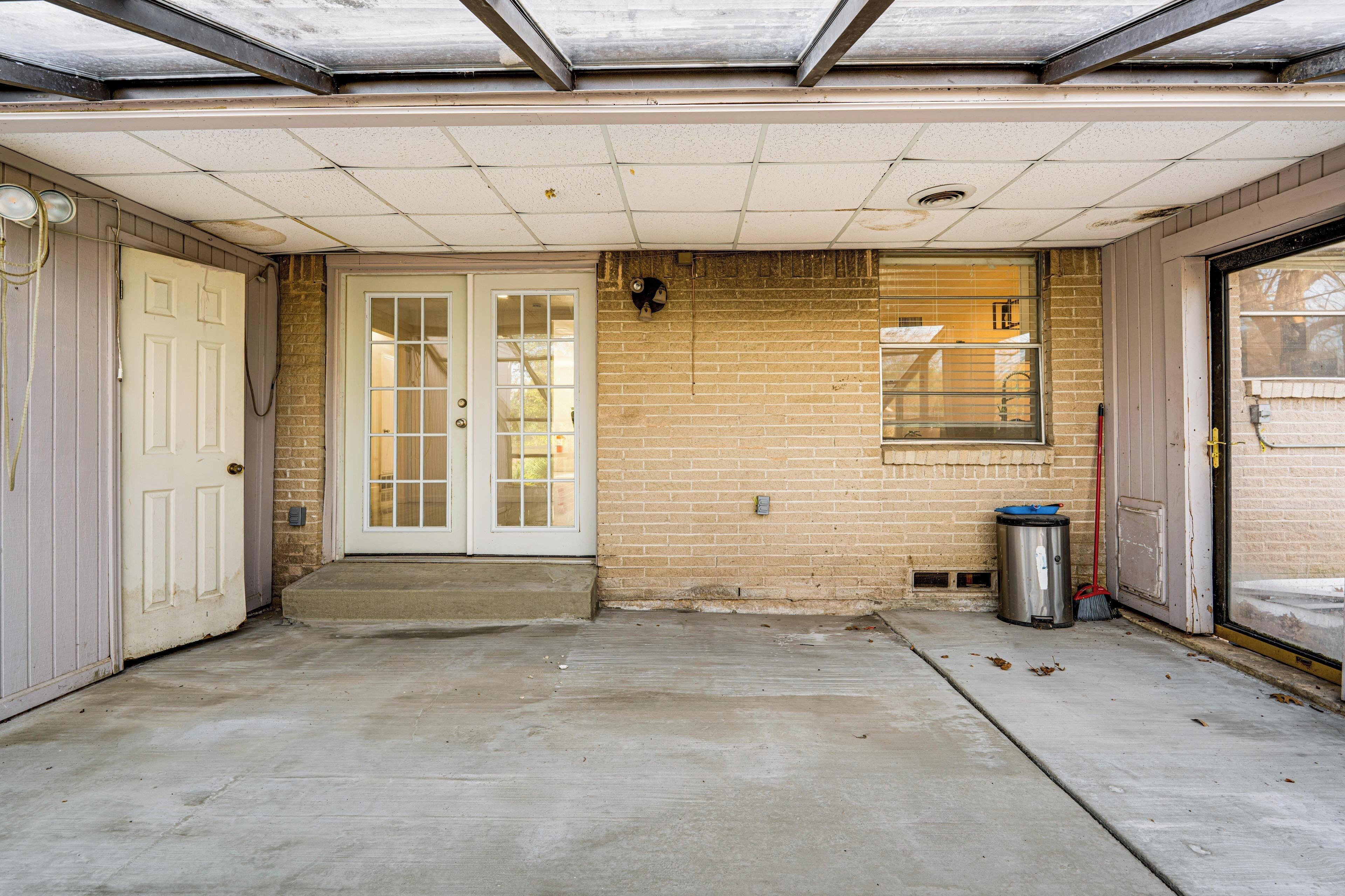 A garage with a concrete floor, a door, a window, and a trash can.