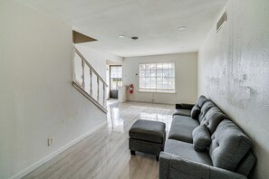 A spacious living room with a grey sectional sofa, a small ottoman, and a staircase leading to another level. - Family + Pet Friendly! Garland Home w/ Fenced Yard (Garland)