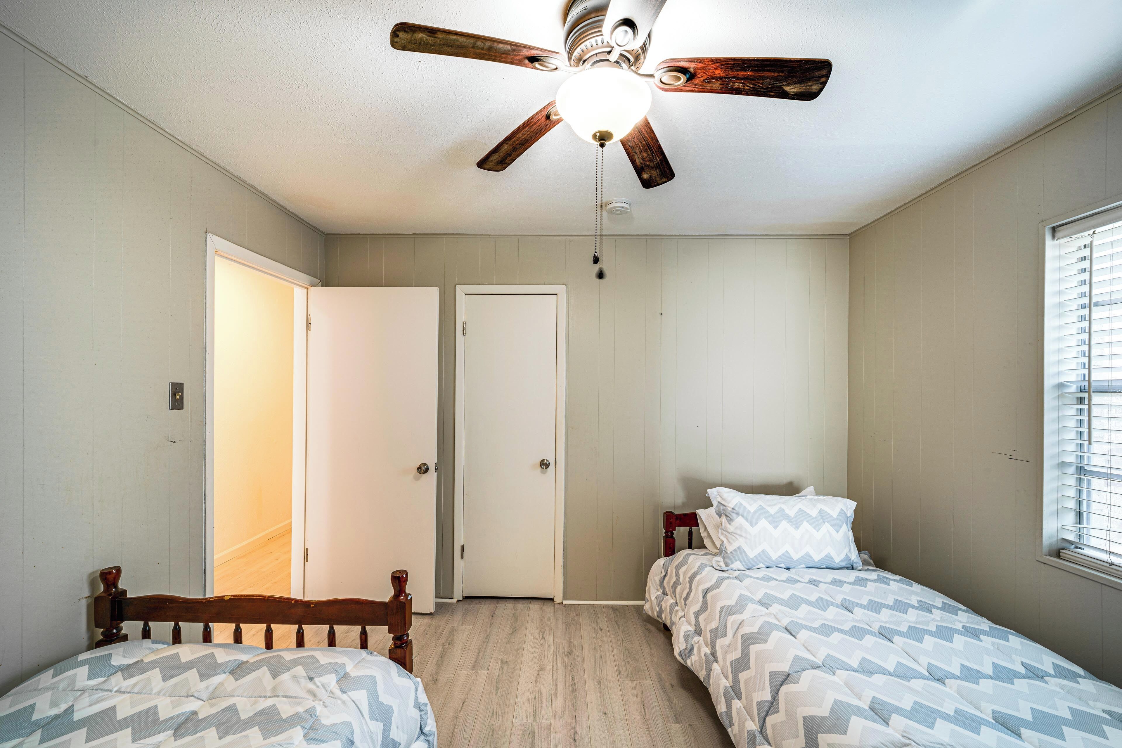 Ein Schlafzimmer mit zwei Betten, einem Deckenventilator und einer Tür zu einem anderen Raum.