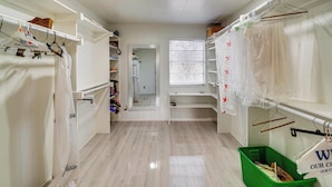 A hotel room with a wooden floor, a closet with hanging clothes, a window with blinds, and a green trash bin. - Family + Pet Friendly! Garland Home w/ Fenced Yard (Garland)