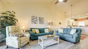 Un salon avec un canapé vert, un fauteuil à motifs floraux et une table basse. On y trouve également une grande plante et des œuvres d’art accrochées au mur.