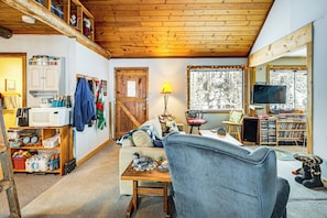 L’intérieur chaleureux d’un chalet avec un plafond en bois, un coin cuisine équipé d’un four à micro-ondes, une table à manger et un téléviseur placé dans un coin.
