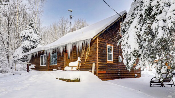 A wooden cabin with a snow-covered roof, surrounded by trees and a bench in the snow. - 4 Mi to Ski Brule: Cozy Cabin w/ Screened-in Porch (Iron River)
