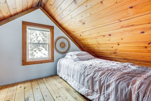 Une chambre avec un plafond en pente, une fenêtre donnant sur des arbres couverts de neige, un lit avec une couverture à rayures et un élément de décoration circulaire sur le mur.