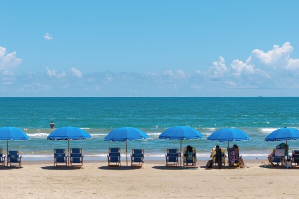 A beach with multiple blue umbrellas and beach chairs. - Resort Condo w/ Gulf Views: Suntide III - Unit 207 (South Padre Island)