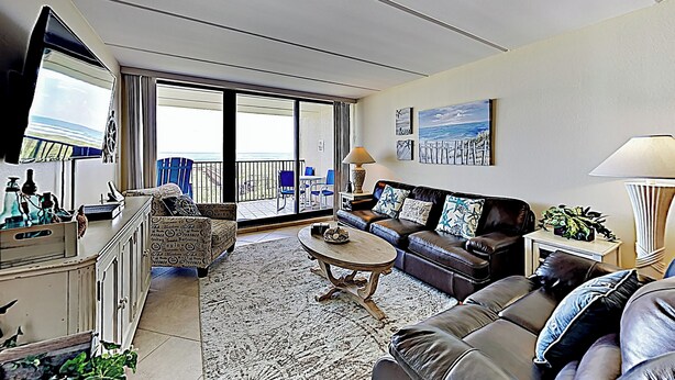 Un soggiorno con divano, tavolino e TV. Un balcone con vista sul mare.