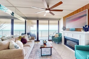 Amplia sala de estar con un ventanal grande, ventilador de techo, chimenea y balcón con barandilla.