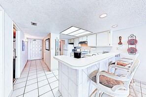 A kitchen with white cabinets, a central island, and a seating area with white chairs. - Coastal Chic Gulf-view 2br: Suntide III - Unit 604 (South Padre Island)