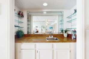 A kitchen with a granite countertop, white cabinets, a stainless steel sink, and a large mirror above the sink. - Coastal Chic Gulf-view 2br: Suntide III - Unit 604 (South Padre Island)