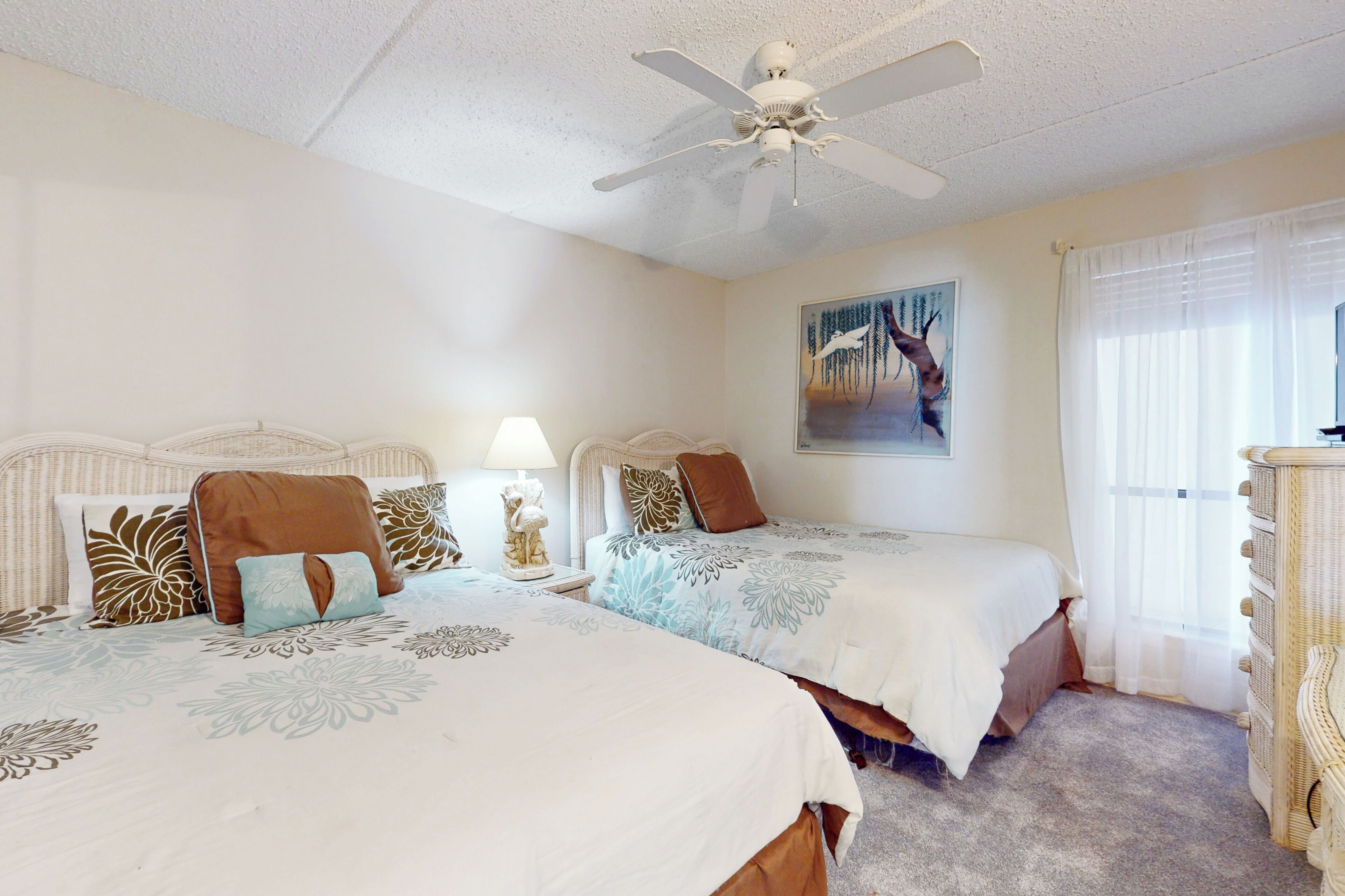 A bedroom with two beds, a ceiling fan, a painting, and a dresser.