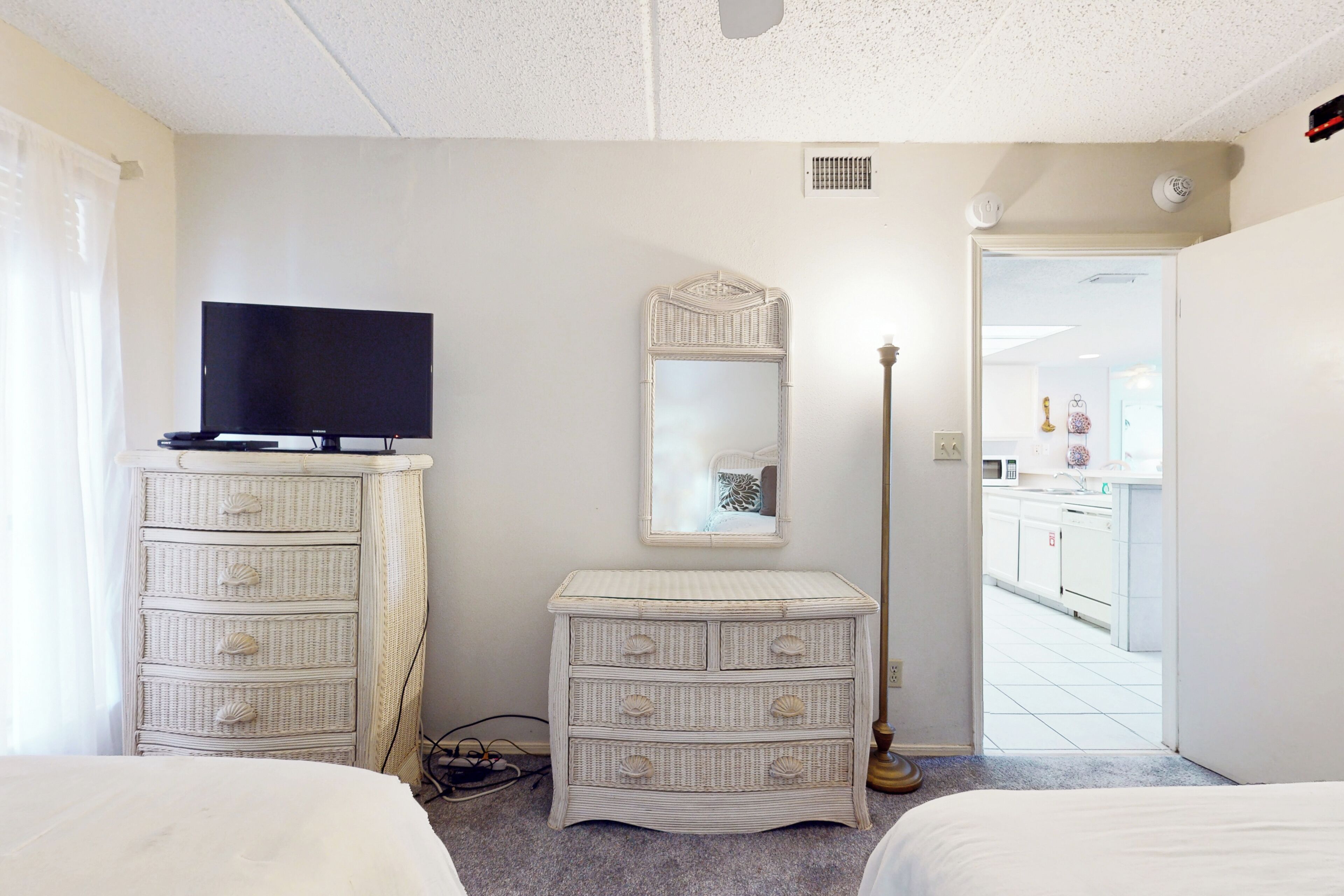 Un dormitorio con televisión, cómoda, espejo y lámpara de pie.