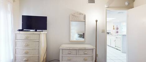 Un dormitorio con televisión, cómoda, espejo y lámpara de pie.