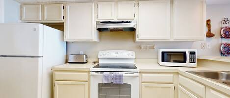 A kitchen with white cabinets, a stove, a microwave, and a refrigerator.