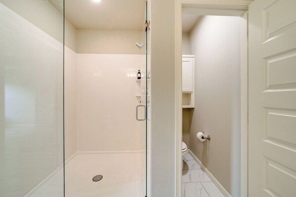 Un baño moderno con cabina de ducha de vidrio, inodoro y puerta blanca.
