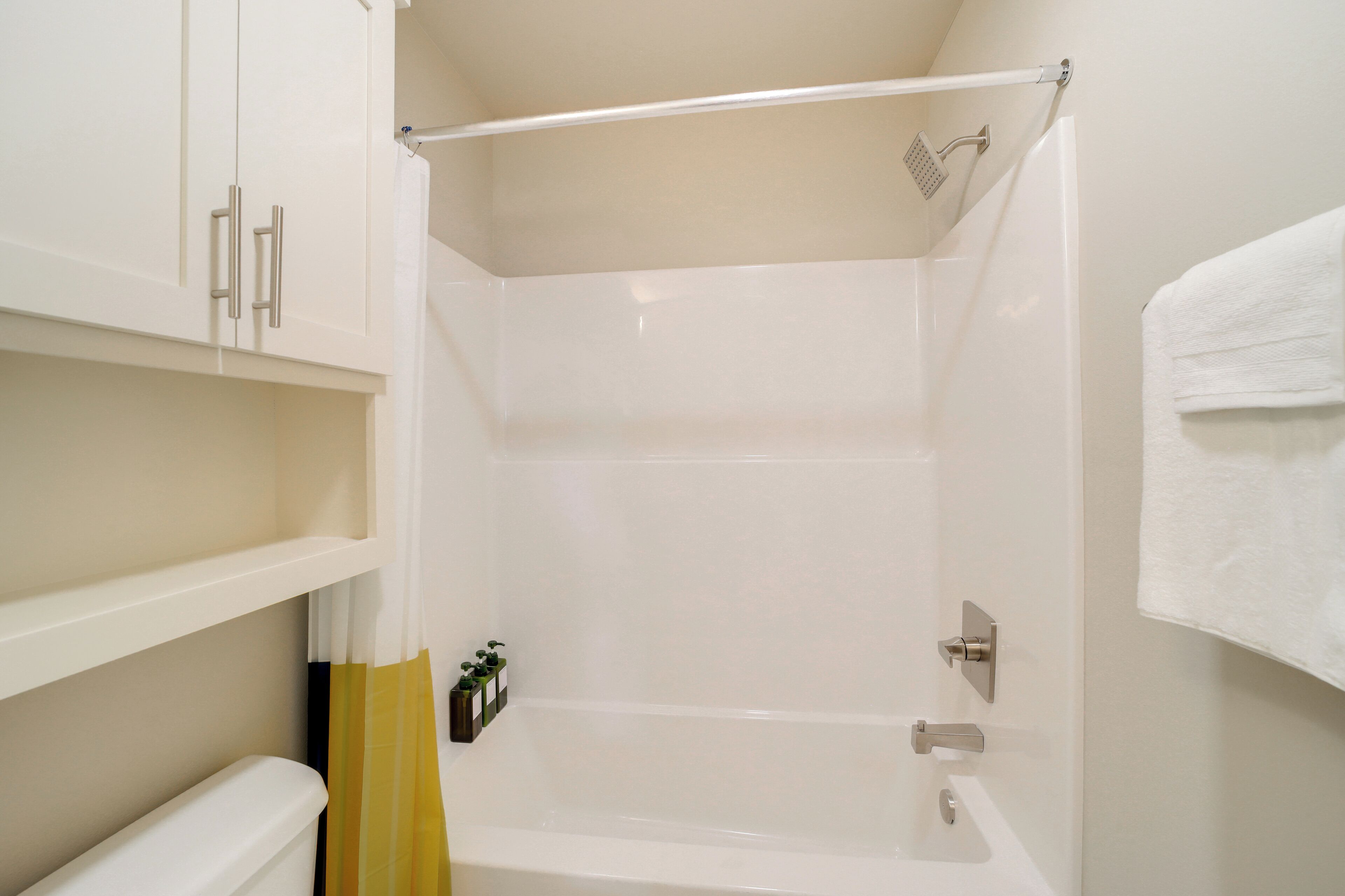 A bathroom with a bathtub, a shower, and a toilet. There are white cabinets and a towel hanging on the wall.