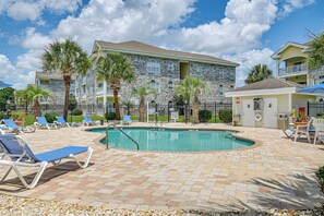 A pool area with lounge chairs, a pool, and a building with stone facade and balconies. - The Magnolia Green: Golf Views, Pool & Patio (Myrtle Beach)
