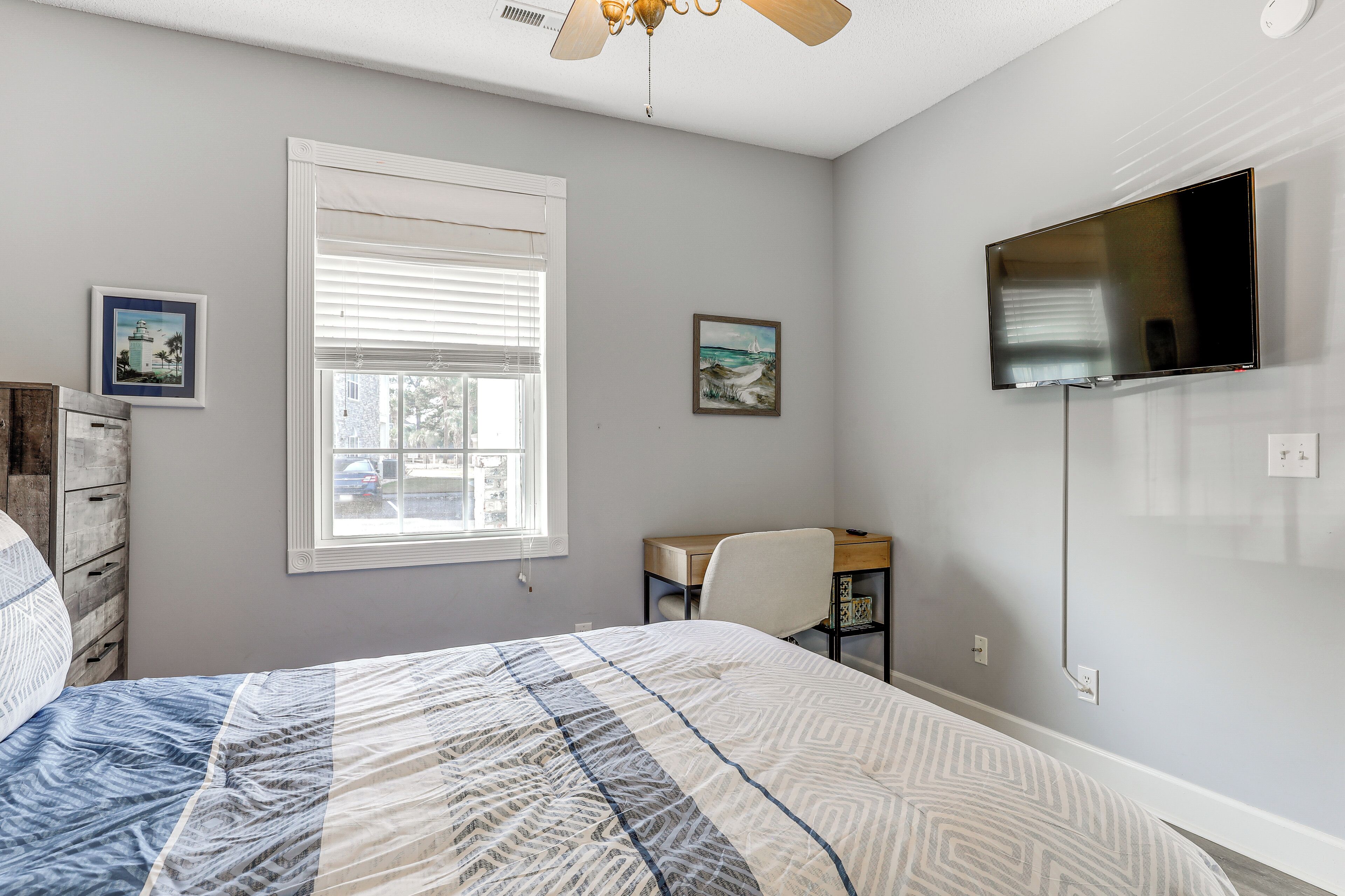 Une chambre à coucher comprenant un lit, un bureau, une chaise, un téléviseur et une fenêtre avec des stores.