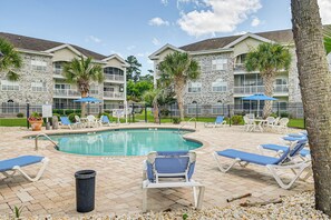 A pool area with lounge chairs and a swimming pool, surrounded by a fence and palm trees. - The Magnolia Green: Golf Views, Pool & Patio (Myrtle Beach)