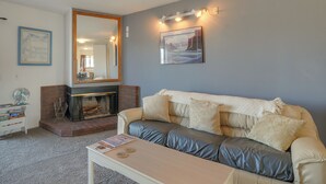 Ett vardagsrum med en beige soffa, en öppen spis, en spegel och en inramad tavla på väggen.
