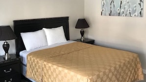 A neatly made bed with a checkered bedspread, a black headboard, two bedside tables with lamps, and a wall-mounted abstract art piece.