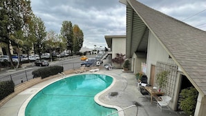 A swimming pool with a curved design, surrounded by a concrete deck. There are lounge chairs and a small table with chairs.
