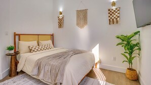 A bedroom with a bed, bedside tables, a wall-mounted TV, and a potted plant. - 5 Mi to Nyc: Bright & Chic Jersey City Getaway! (Jersey City)