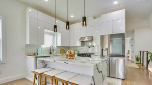 A modern kitchen with white cabinets, a marble island, stainless steel appliances, and wooden bar stools. - 5 Mi to Nyc: Bright & Chic Jersey City Getaway! (Jersey City)
