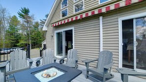 Een terras met Adirondack stoelen, een vuurkorf en een huis met rood en wit decor.