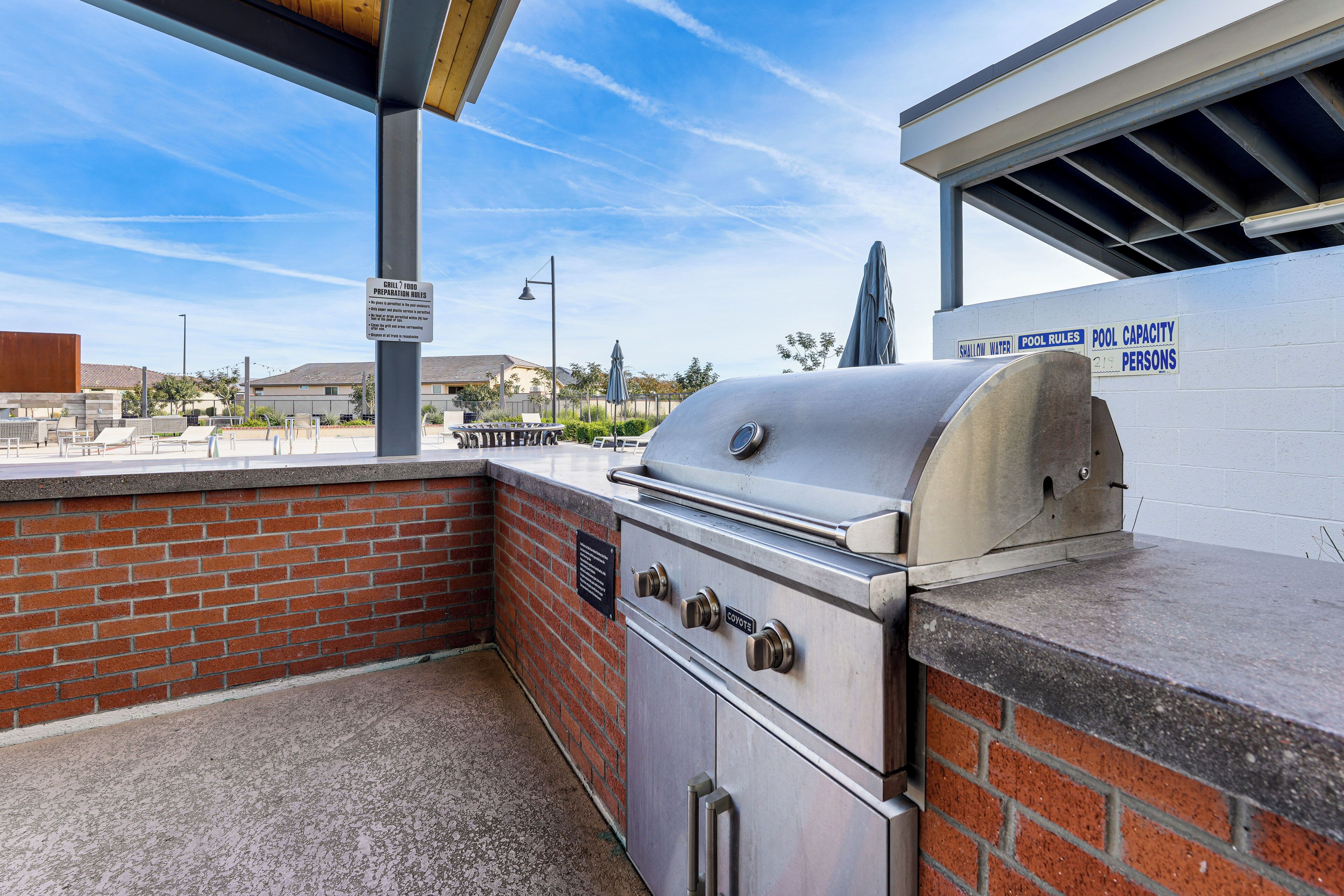 An outdoor grill area with a brick wall and a sign indicating pool rules and capacity.