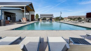 Un área de piscina con sillones reclinables, una zona de estar techada y un edificio con techo inclinado.
