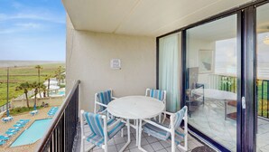A balcony with a white table and chairs, overlooking a pool and a view of the beach. - 2BR w/ Luxury Resort Perks: Suntide III - Unit 507 (South Padre Island)