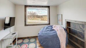 Una camera da letto con una grande finestra, un letto, una televisione e un tavolino.