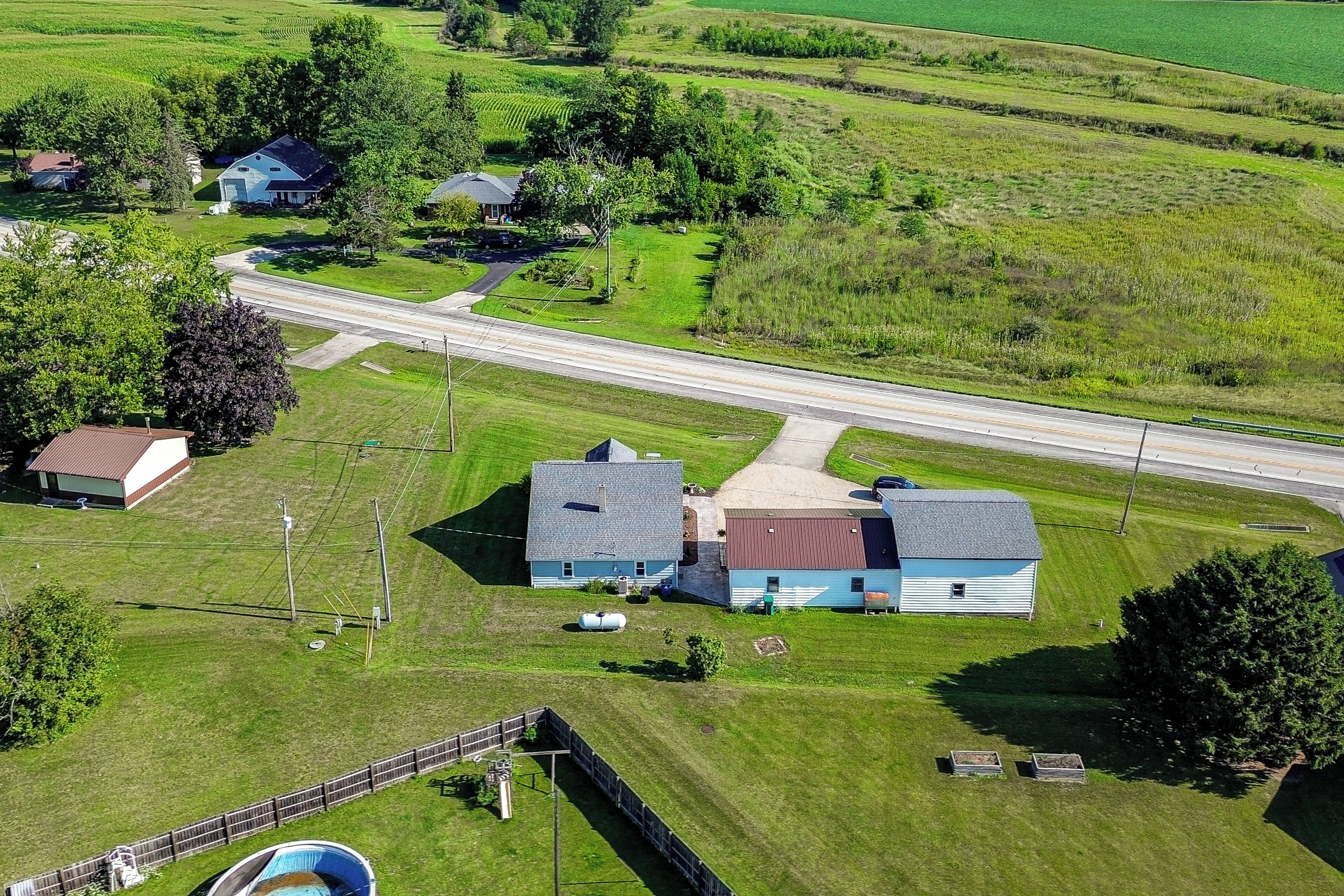 A rural landscape with a road, houses, and a fenced area.