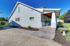 Une maison de plain-pied avec un toit en pente, une véranda et un jardin devant, avec une allée en gravier et des aménagements paysagers.