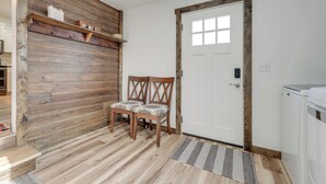 Una stanza con rivestimenti in legno, una porta bianca, due sedie di legno, un tavolino e una lavatrice.